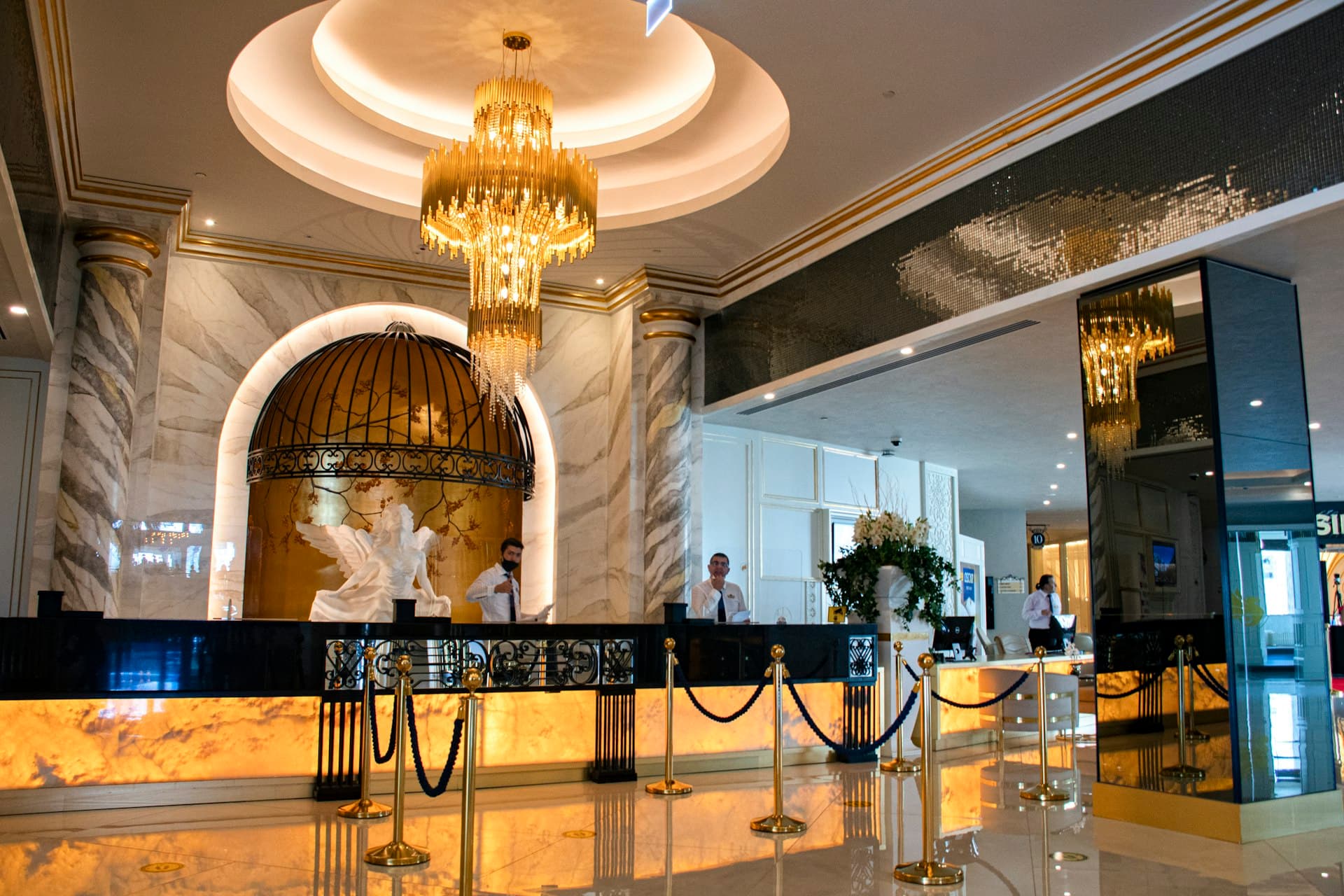 Grand hotel lobby with marble reception desk, gold chandelier, and uniformed staff